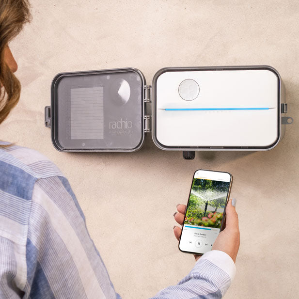 Outdoor Rachio Smart Sprinkler Controller with woman holding smart phone showing Rachio App Quick Run.